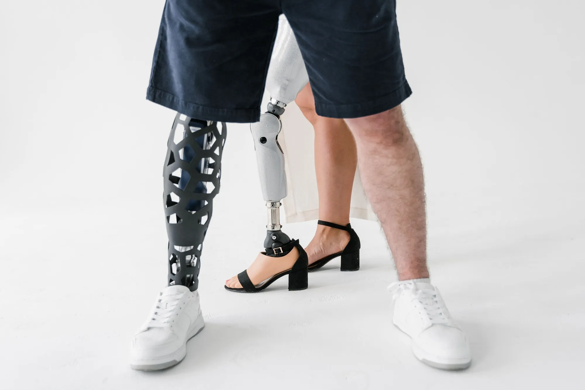 Close-up of two prosthetic legs and shoes against a white background.
