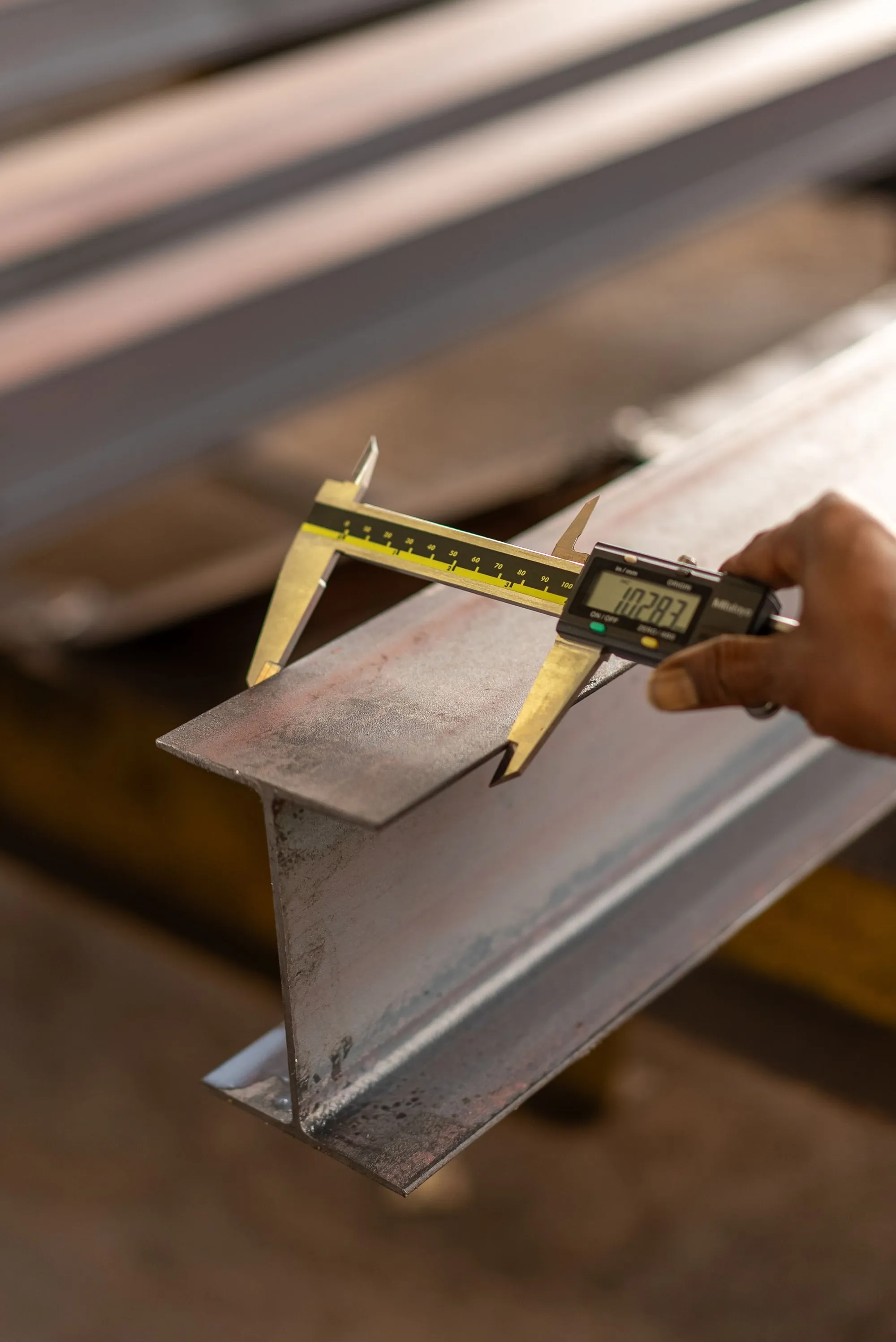 A digital caliper held across a metal beam.