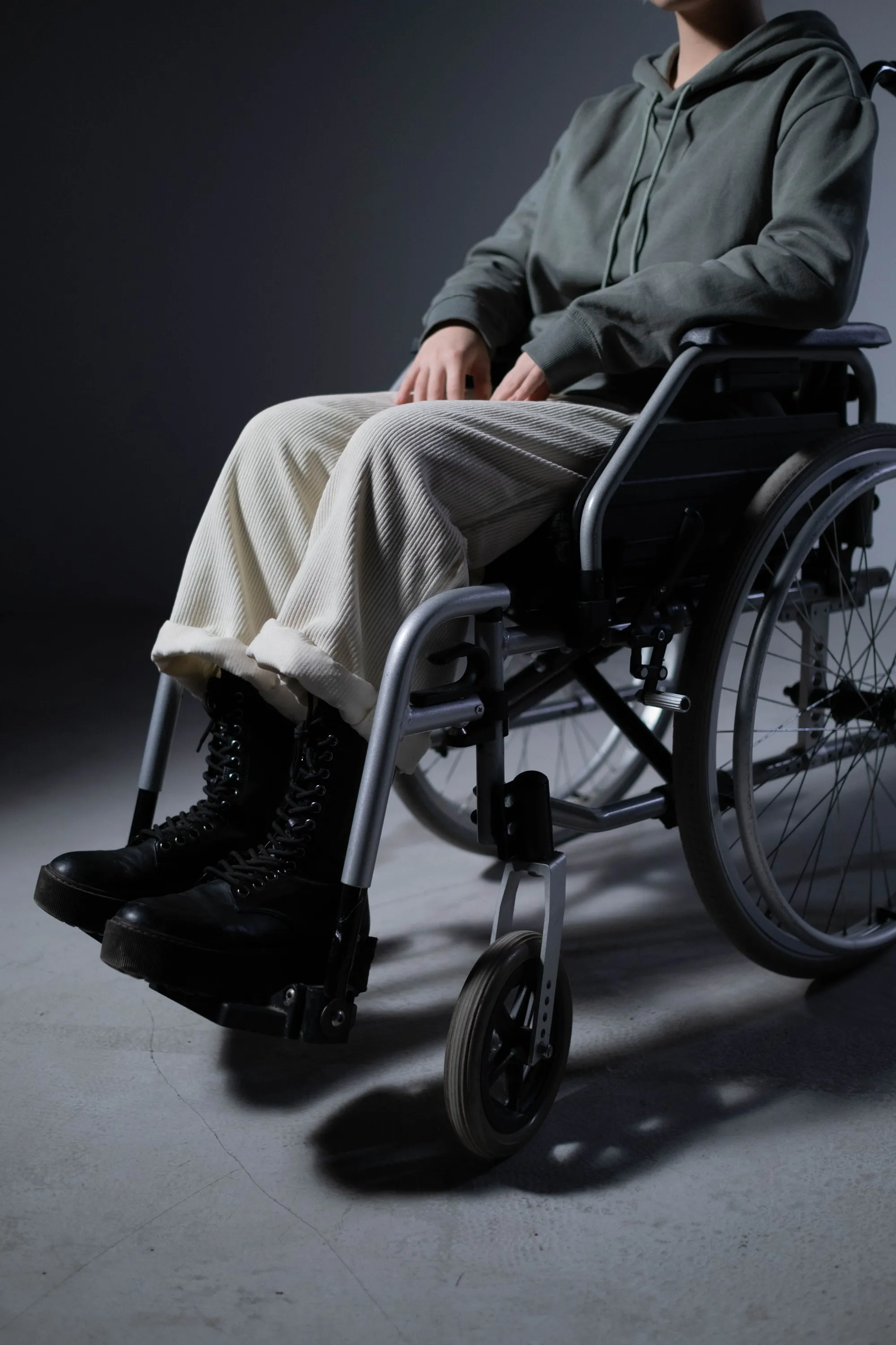 A seated person's hands, legs and wheelchair in a studio close-up.