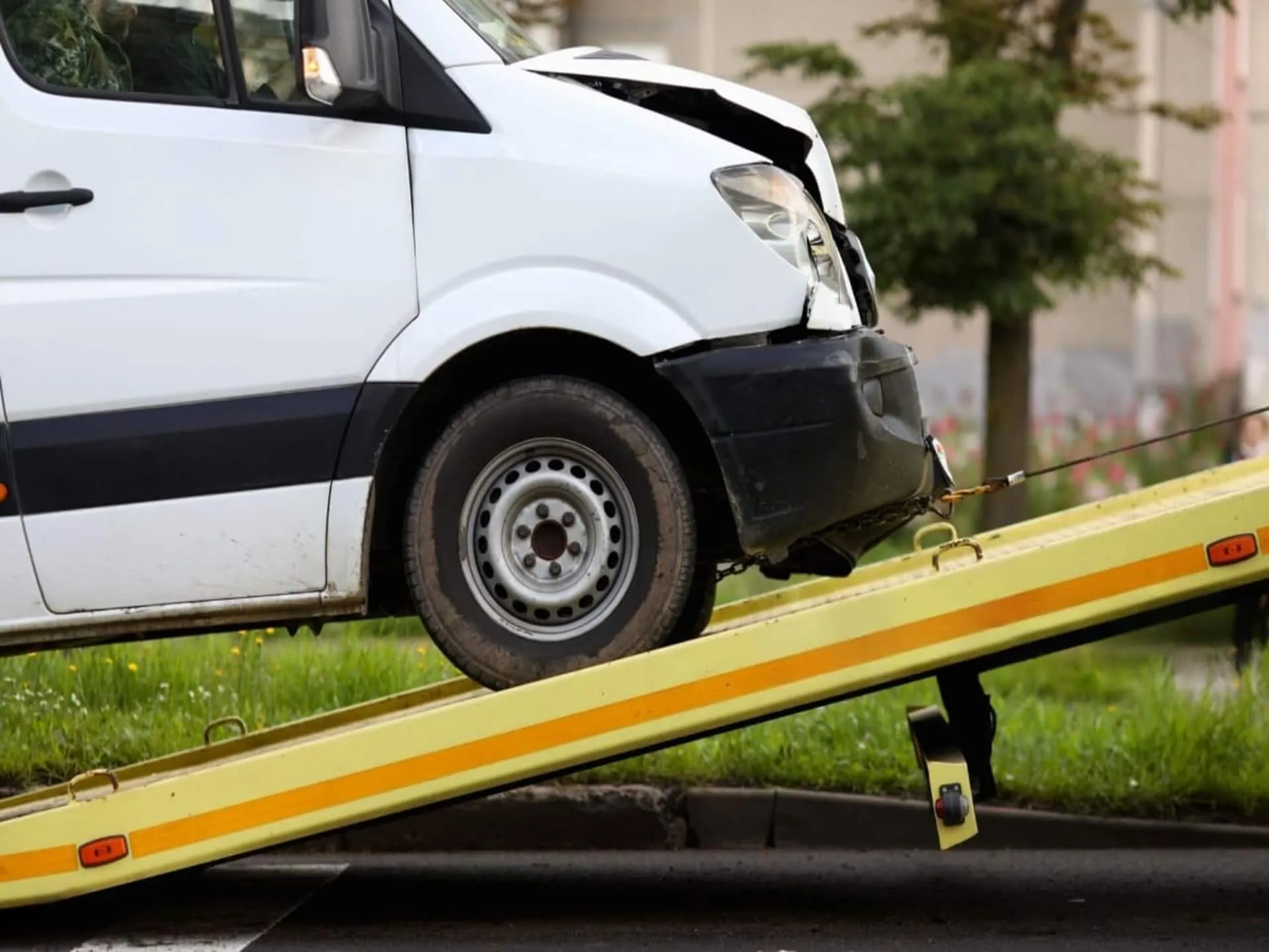 A damaged white cargo van being loaded onto a recovery vehicle.