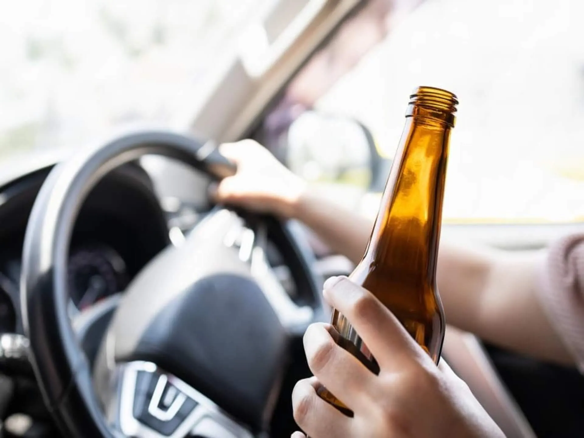 A driver holding a beer bottle at the steering wheel.