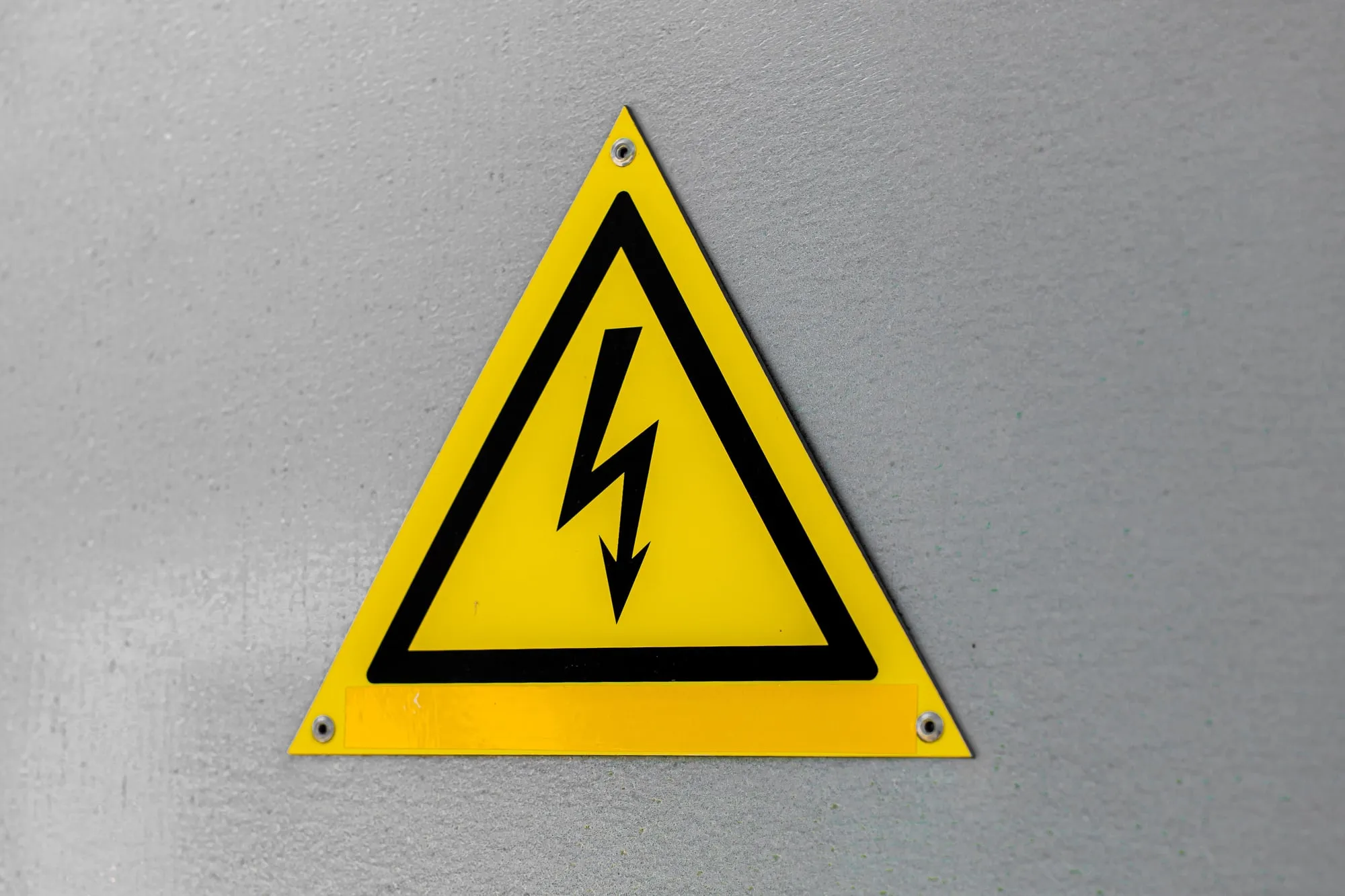 A yellow triangular electrical warning symbol on a gray wall.