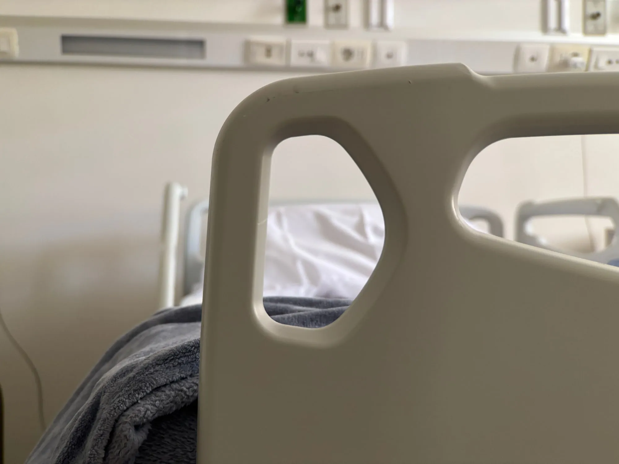 An empty hospital bed with linens and a raised side rail.