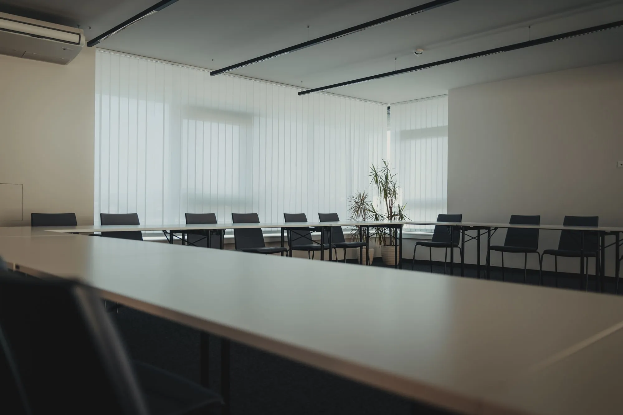 Tables and empty chairs in a meeting room with large windows.
