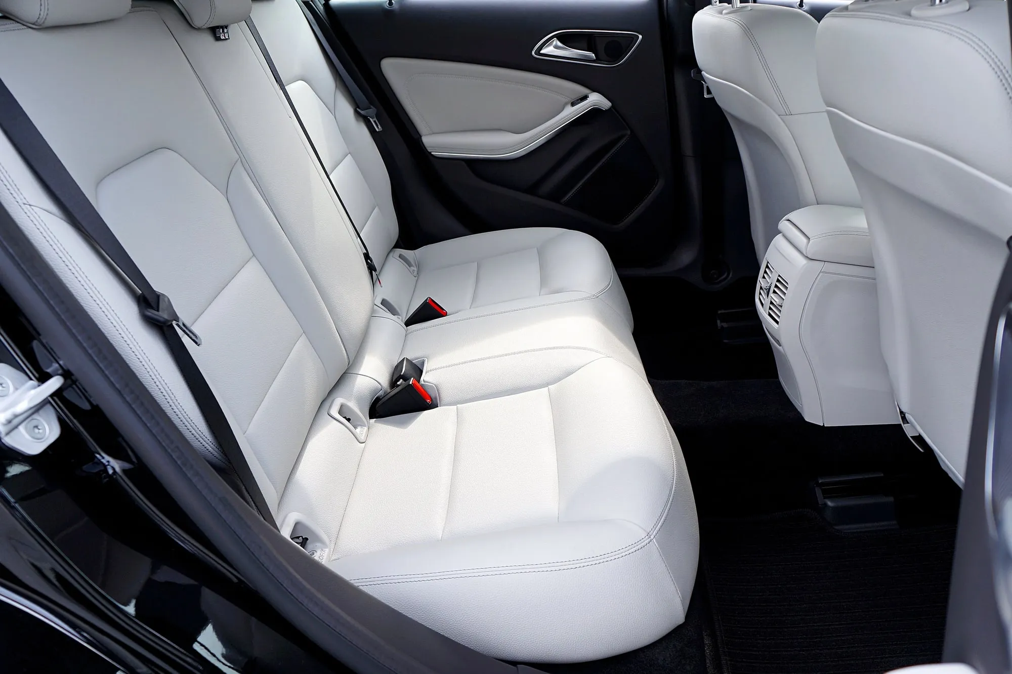 Empty white rear passenger seats and seat belts inside a car.