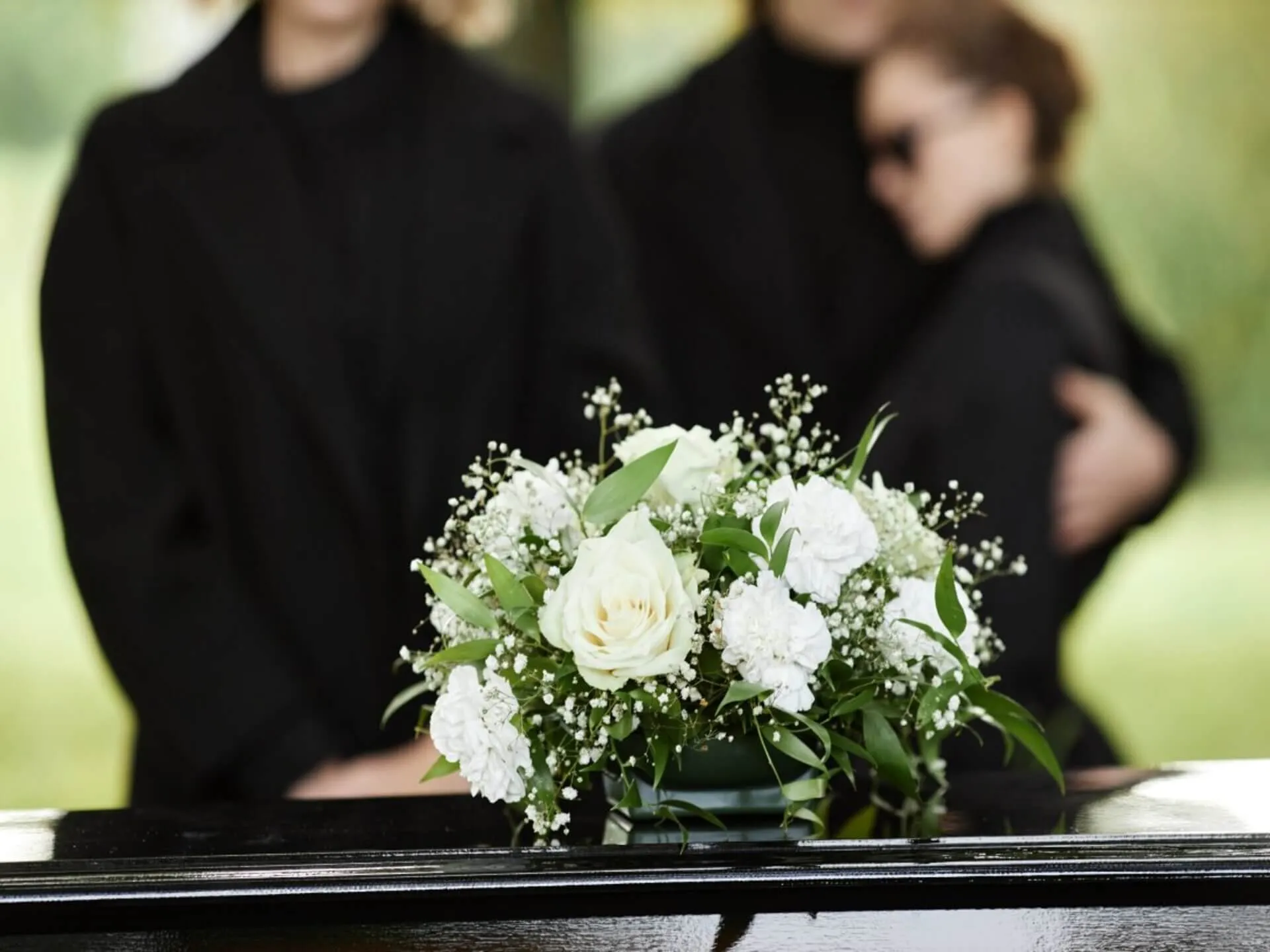A white floral arrangement on a casket with people in the background.