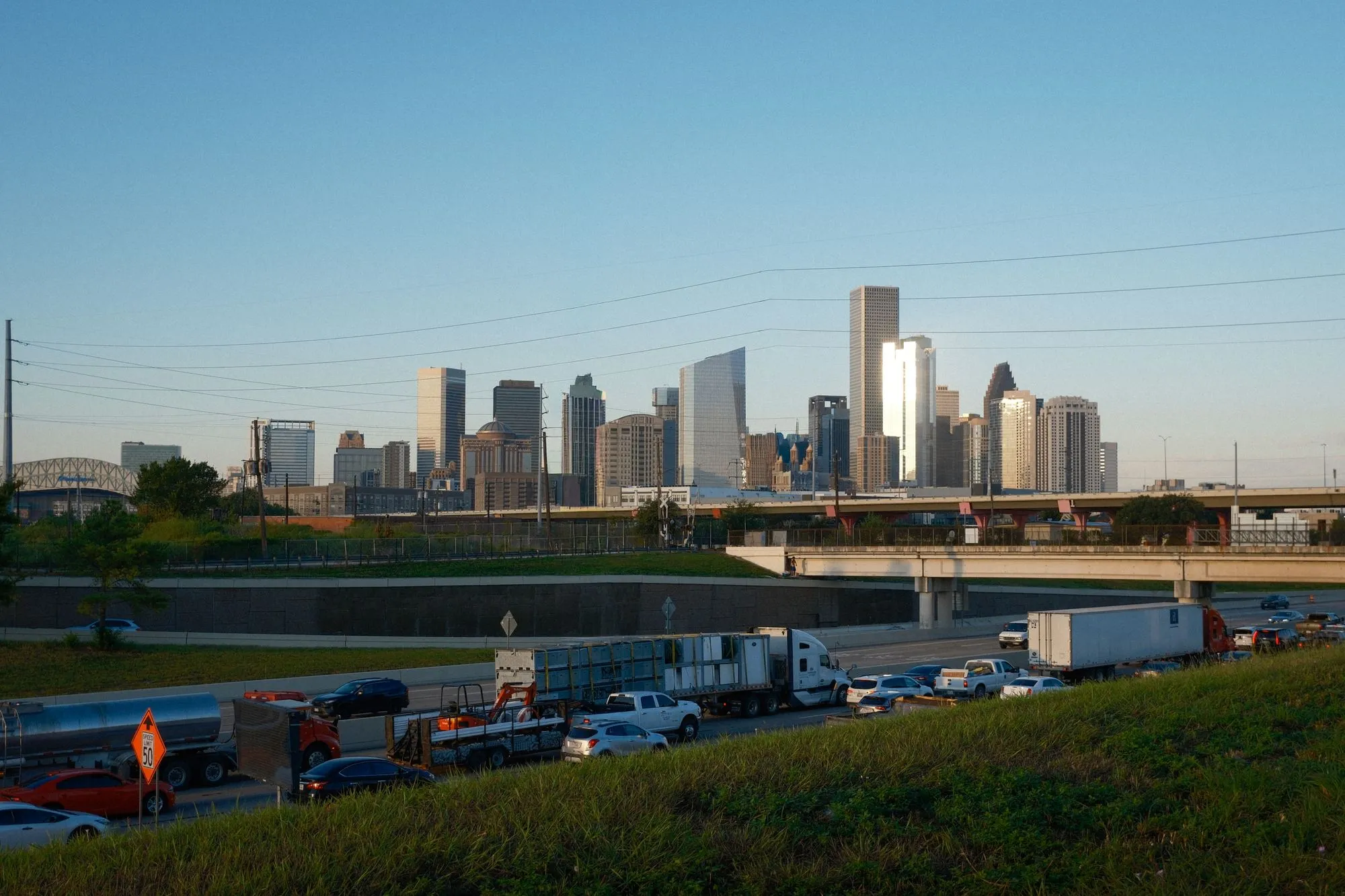 Downtown Houston's skyline behind a freeway crowded with semi-trucks, trailers, and cars.