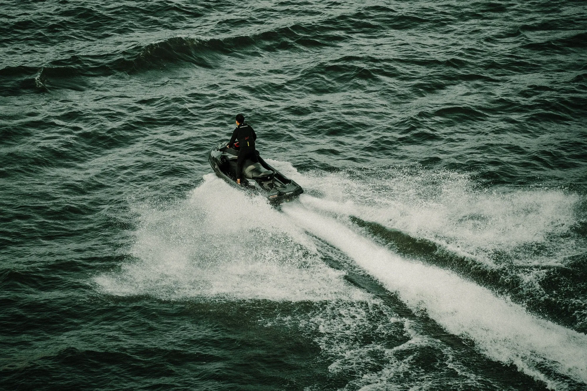 A personal watercraft and its rider seen from above and behind, leaving a wake.