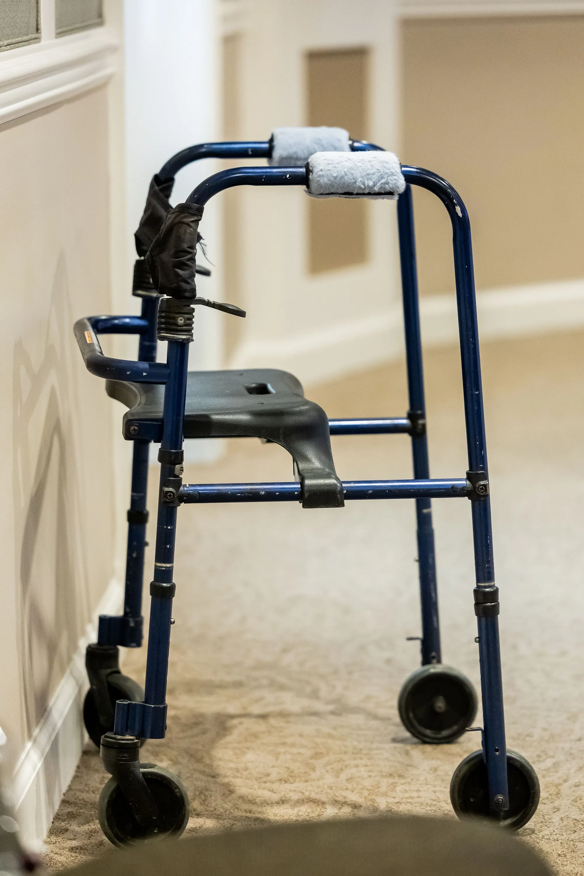 A blue rolling walker beside a wall in a carpeted hallway.