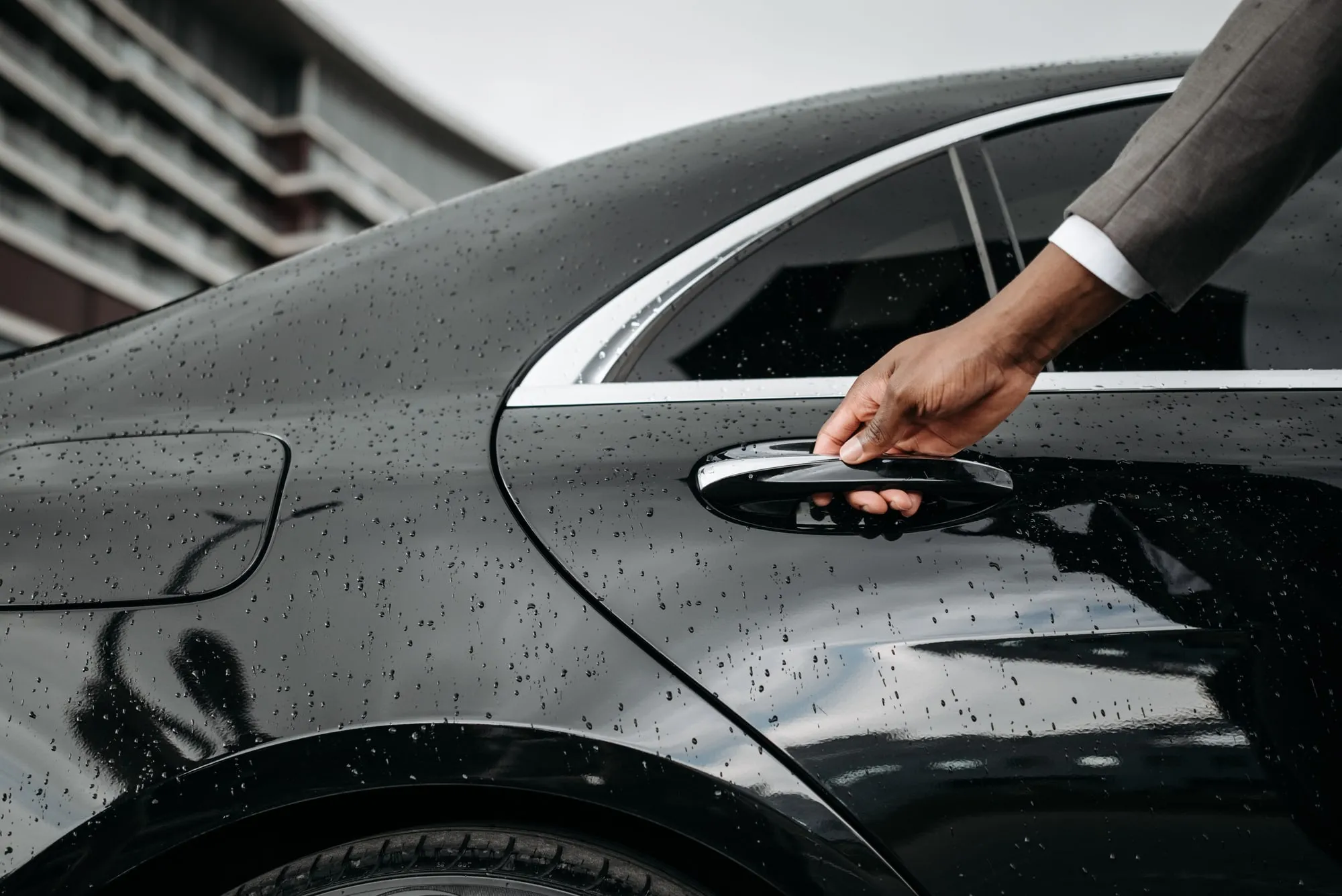 A hand opening a black car door in the rain.