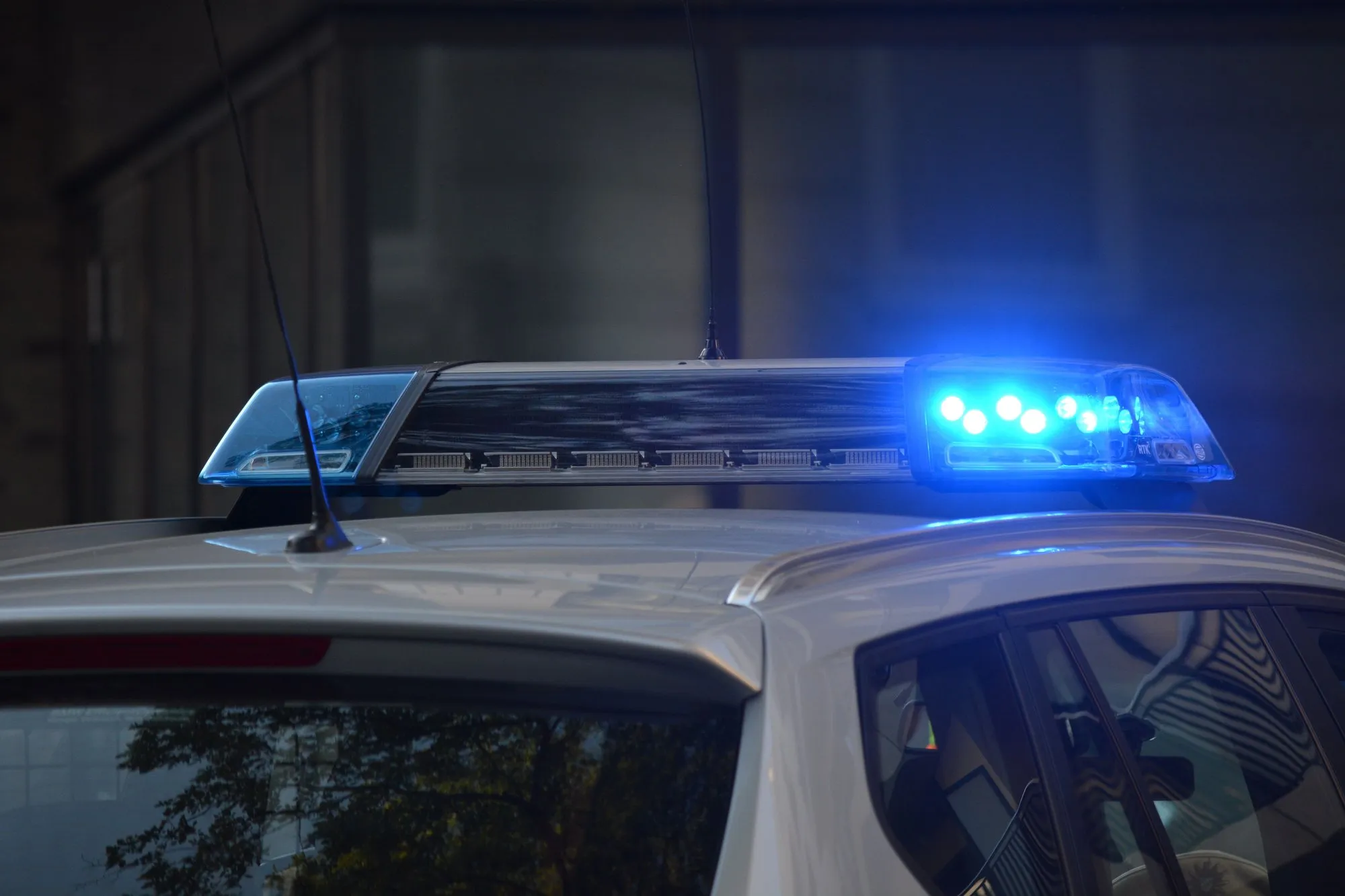 A police car’s roof light bar with its blue lights flashing at dusk.