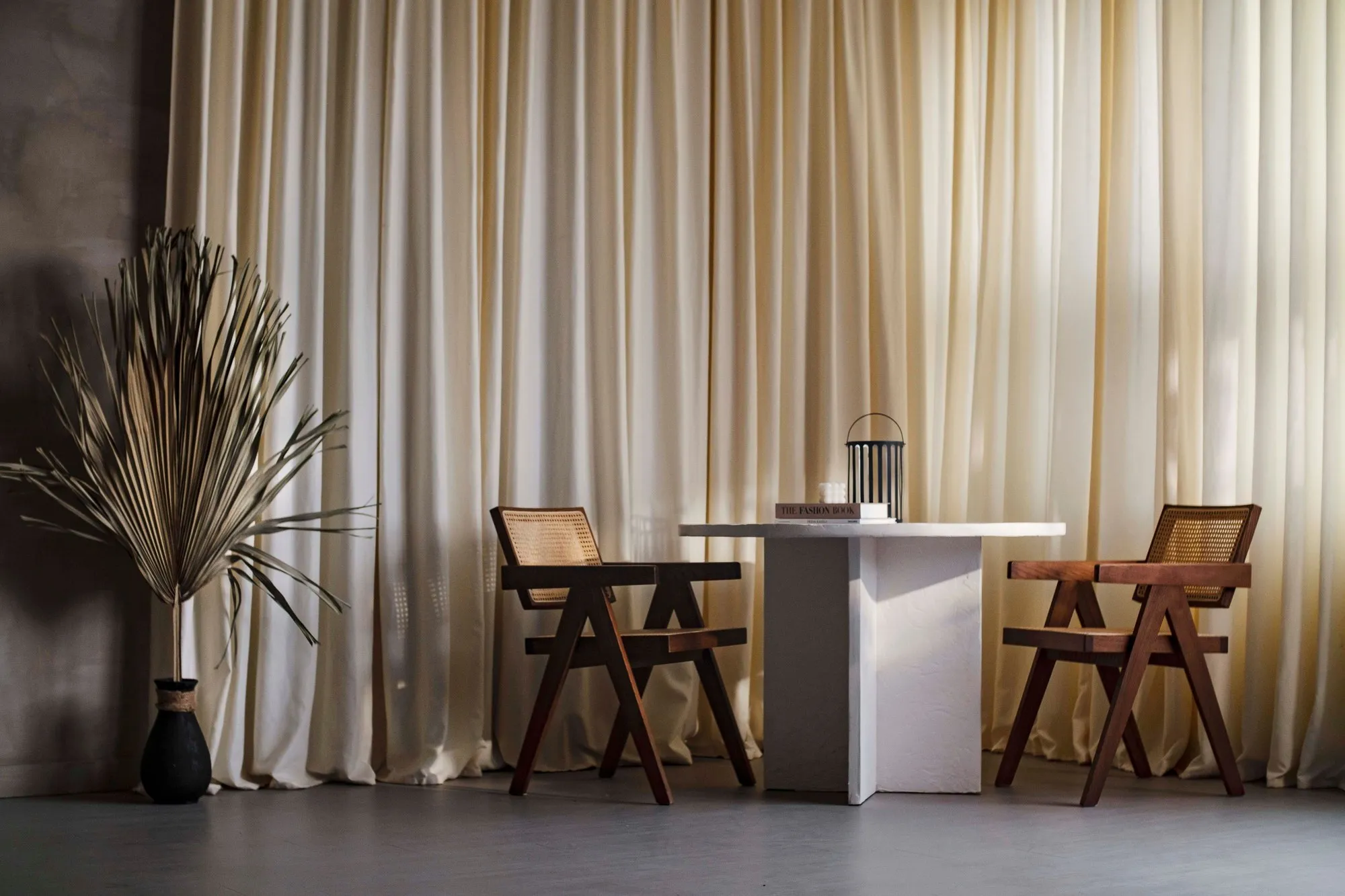 Two empty wooden armchairs facing a small table in front of curtains.