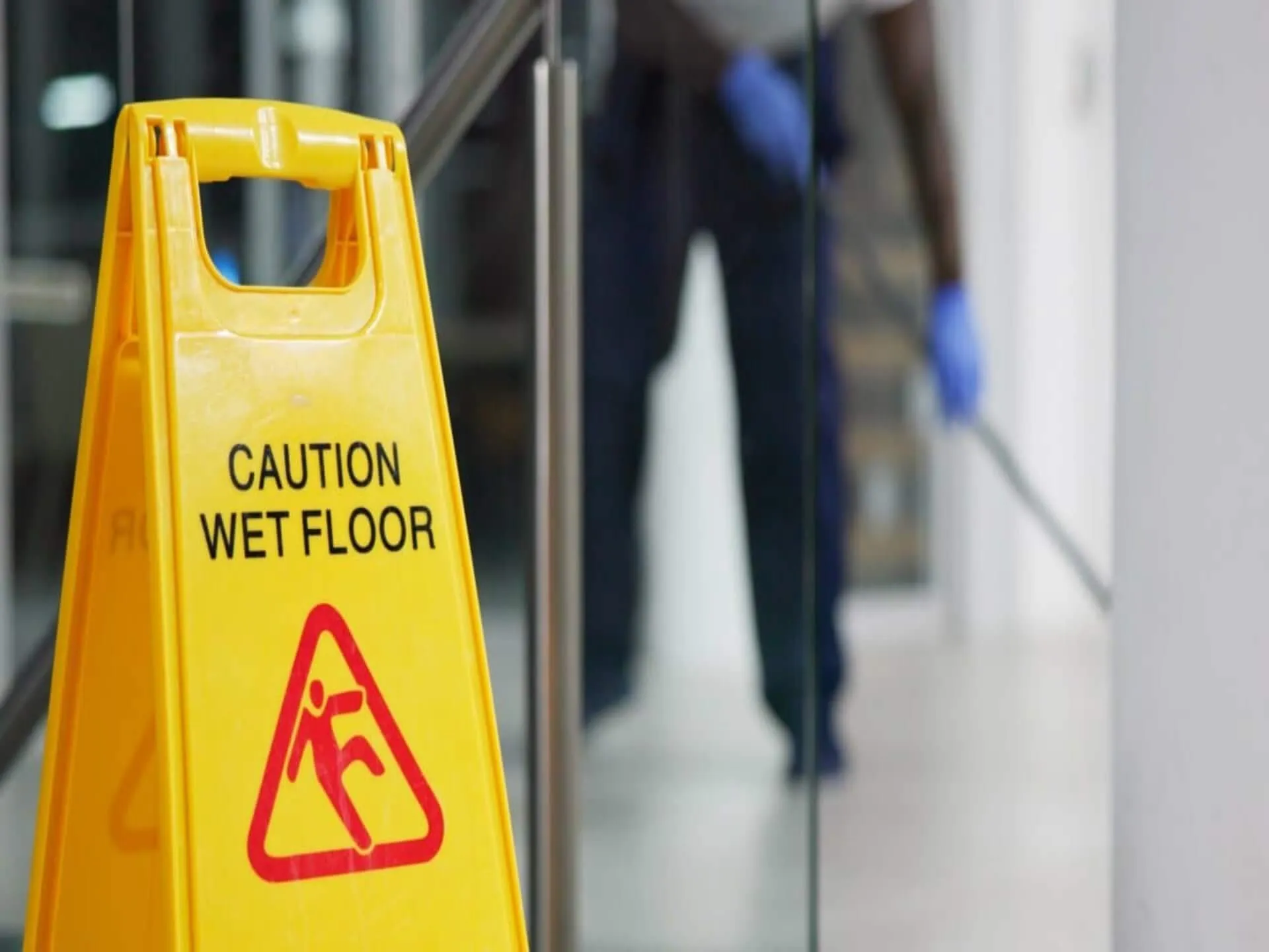 A wet-floor warning sign with a cleaner in the background.