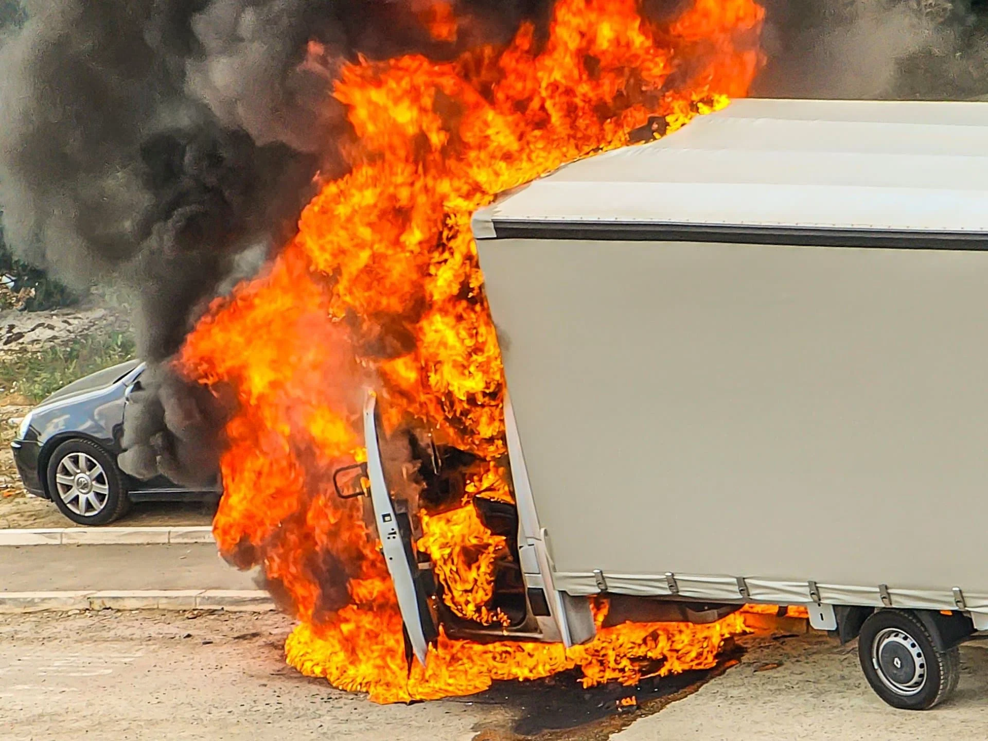 A box truck engulfed in flames beside a roadway.